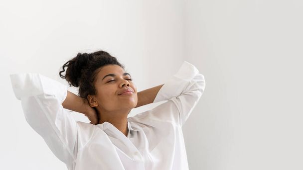 Kafasını kapalı gözlerle geri atan barışçıl Afro-Amerikan genç kız portresi. İşten sonra dinlen. Mutlu hissediyorum. Huzur ve mutluluk kavramı - Fotoğraf, Görsel