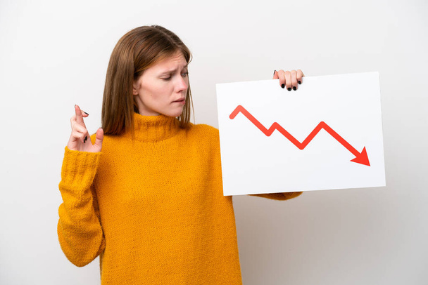 Young English woman isolated on white background holding a sign with a decreasing statistics arrow symbol with fingers crossing - Фото, зображення