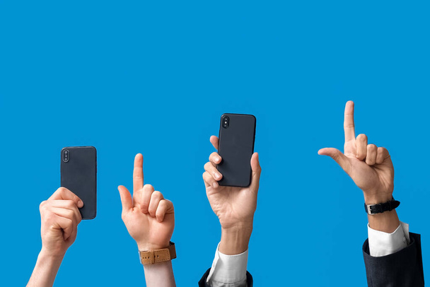 Hombres de negocios con teléfonos móviles apuntando a algo sobre fondo azul - Foto, imagen