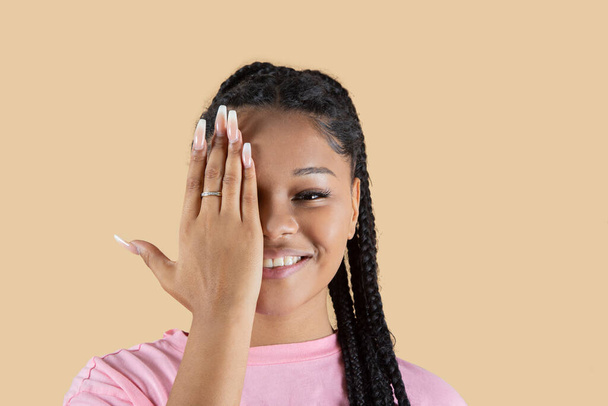 mujer feliz hispana cubre un ojo con su mano, sobre fondo beige - Foto, imagen