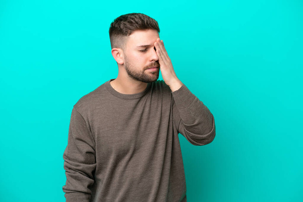 Young caucasian man isolated on blue background with headache - Фото, зображення