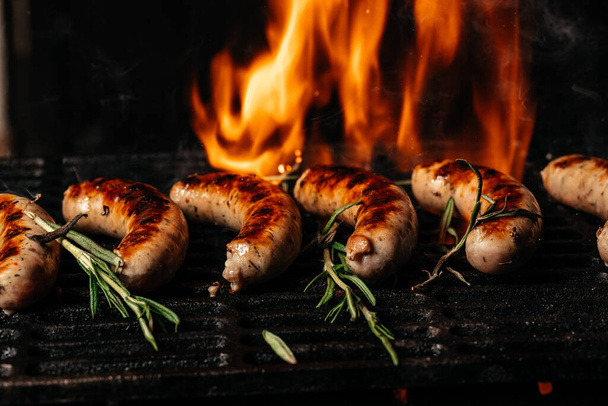 Жареные колбасы на гриле с дымом и пламенем на темном фоне, Концепция приготовления мяса. Фон рецепта еды. Закрывай. место для текста, - Фото, изображение