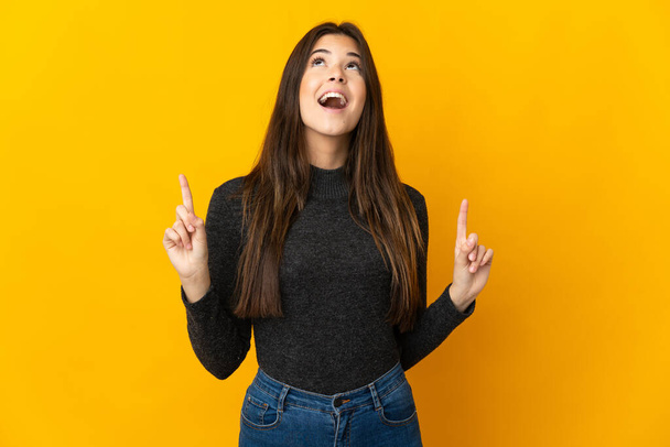 Teenager Brazilian girl isolated on yellow background surprised and pointing up - Foto, Imagem