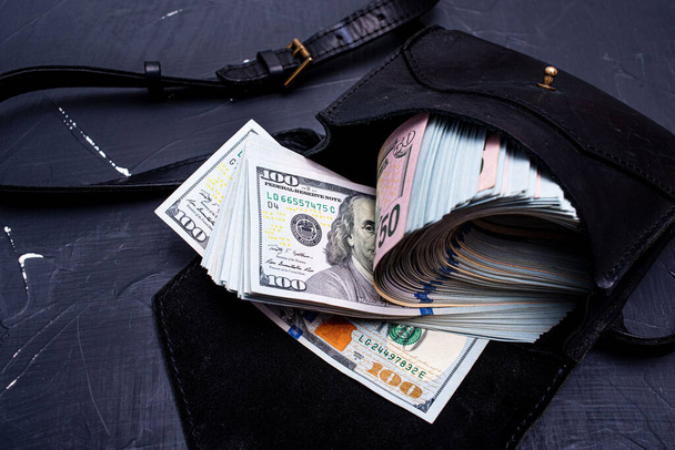 Business concept. Dollars in a black leather bag on a black cement background. - Photo, Image