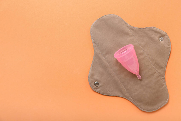 Herbruikbare menstruatiepad en beker op oranje achtergrond - Foto, afbeelding