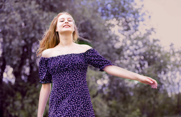 Happy young girl in a romantic dress on a green summer meadow. Beautiful teen girl smiles and looks into the camera. - 写真・画像