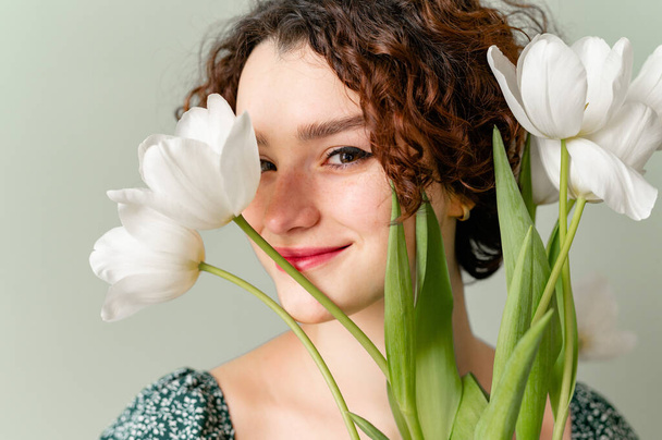 teenage girl with curls on a gray background with tulips smiling - Photo, Image