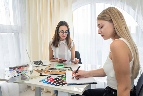 belles jeunes filles collègues envisageant une palette de couleurs pour les chambres design avec ordinateur portable à la table. Concept de conception - Photo, image