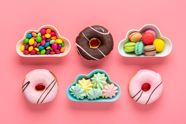 édességek és habcsók tál alakú felhő, csokoládé színes feltét és rózsaszín fánk elszigetelt rózsaszín háttér Lapos feküdt Felülnézet Knolling Egészségtelen és ízletes élelmiszer koncepció. - Fotó, kép