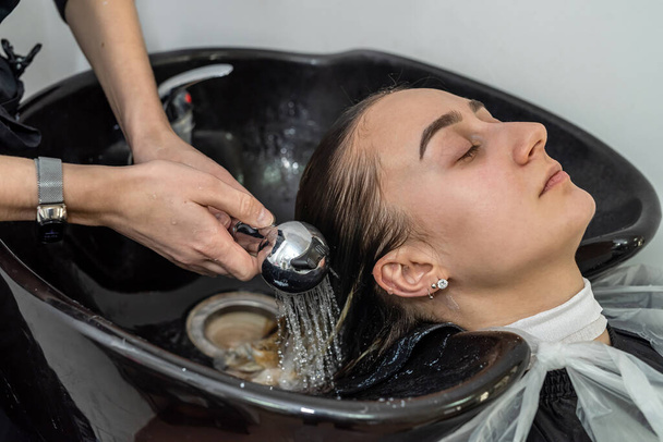 pätevä viileä hiusmestari pesee asiakkaan pään hiusten vaalentamisen jälkeen. Käsite pesu tytön pään - Valokuva, kuva