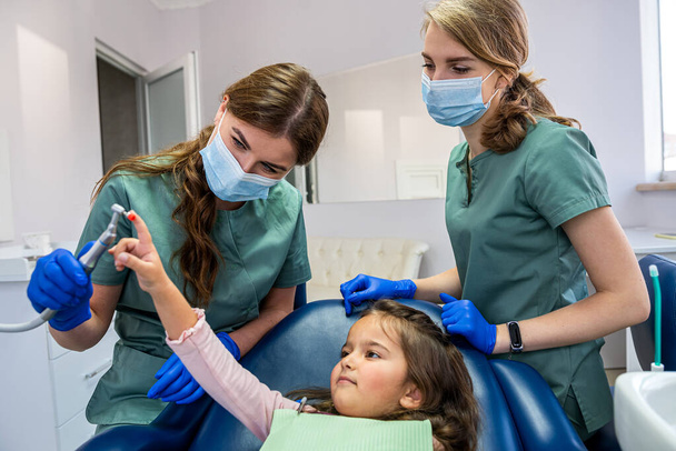 молодая квалифицированная стоматолог-специалист, чистившая зубы маленькому ребенку, которого привезли на прием. Концепция чистки молочных зубов - Фото, изображение