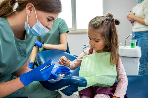 νεαρή ειδικευμένη οδοντίατρος που βουρτσίζει τα δόντια ενός μικρού παιδιού που μεταφέρθηκε στη δεξίωση. Η έννοια του βουρτσίσματος των δοντιών του μωρού - Φωτογραφία, εικόνα