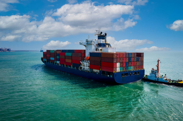  containerschip zeilen in groene zee en sleepboot slepen en blauwe lucht achtergrond van drone schot  - Foto, afbeelding