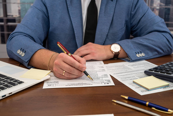 handsome male businessman sitting at the table and filling out US tax forms 1040. Concept of tax forms and businessman - 写真・画像