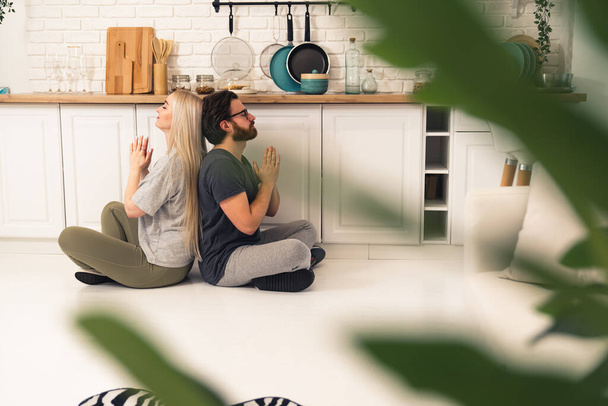 loto de meditación espalda con espalda practicado por una mujer caucásica de pelo largo y su novio en su piso compartido - Foto, Imagen
