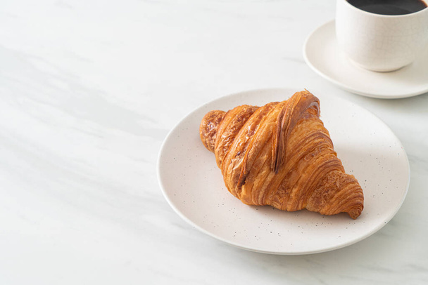 frisches Croissant auf weißem Teller mit schwarzem Kaffee - Foto, Bild