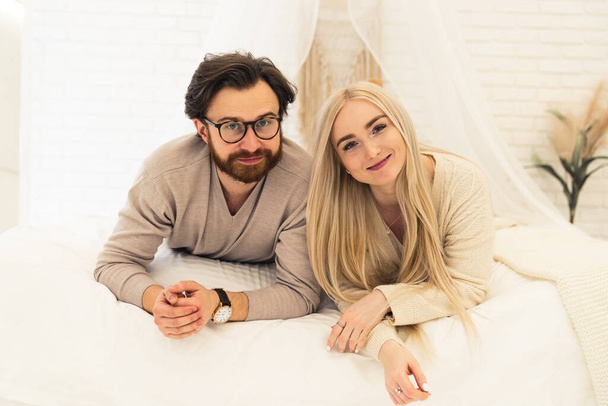 young entrepreneur and his beautiful businesswoman girlfriend laying down on their bed, smiling, and looking at camera - Fotoğraf, Görsel