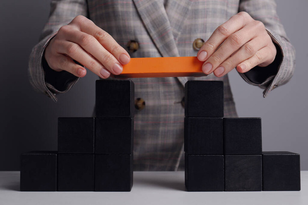 Businesswoman building bridge with colorful blocks at table, closeup. Connection, relationships and deal concept - Foto, afbeelding