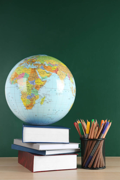 Globe, school supplies and books on wooden table near green chalkboard. Geography lesson - Фото, зображення