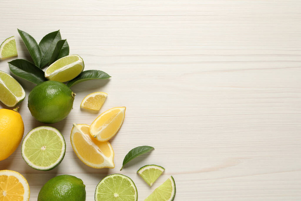 Fresh ripe lemons, limes and green leaves on white wooden background, flat lay. Space for text - Foto, Bild