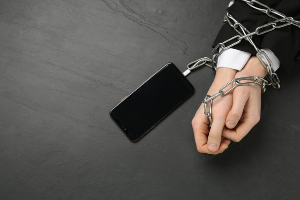 Man showing chained hands to smartphone at black table, top view. Internet addiction - Foto, Bild
