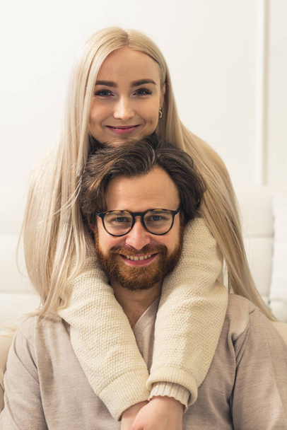 Boldog európai pár koncepció. Millenniumi szőke, hosszú hajú nő ölelgeti a barna szakállú partnere fejét, aki előtte ül. Függőleges lövés. - Fotó, kép