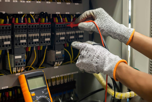 Inżynier elektryk wykorzystuje multimetr do testowania prądu instalacji elektrycznej i przewodu zasilającego w szafie sterowniczej układu elektrycznego. - Zdjęcie, obraz