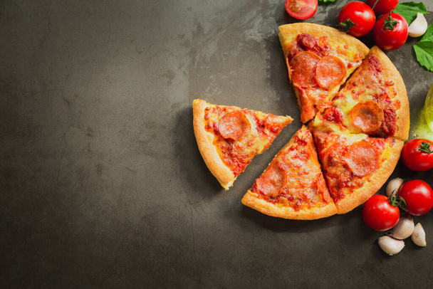 Top view of hot pepperoni pizza,Tasty pepperoni pizza and cooking ingredients tomatoes basil on black background. - 写真・画像