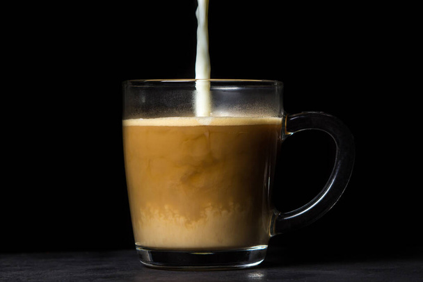 Крем наливают в кофе на черном фоне. Кофейный напиток. Кофе с молоком - Фото, изображение