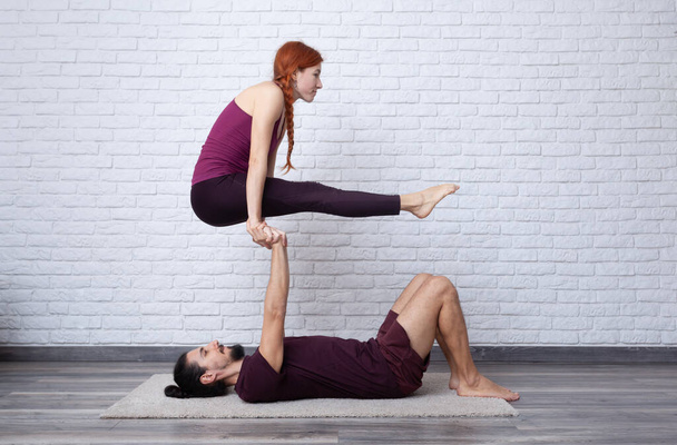 Νεαρό ζευγάρι που διασκεδάζουν στο σπίτι με κάποιες πόζες acro yoga σε διάφορα μέρη. - Φωτογραφία, εικόνα