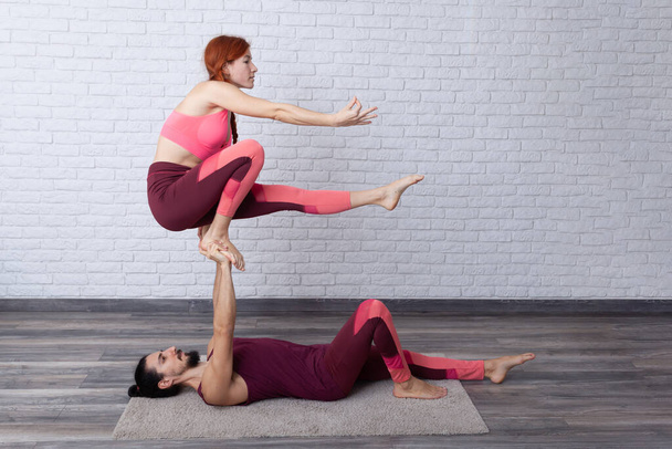 Νεαρό ζευγάρι που διασκεδάζουν στο σπίτι με κάποιες πόζες acro yoga σε διάφορα μέρη. - Φωτογραφία, εικόνα