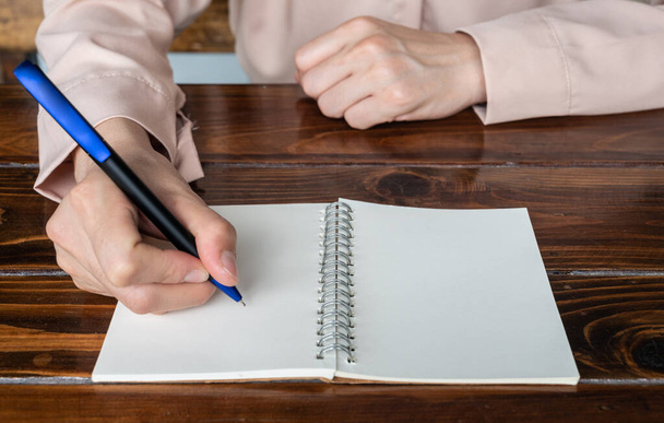 Primo piano di una donna che tiene una penna per scrivere qualcosa o un messaggio su carta bianca vuota in un libro aperto. - Foto, immagini