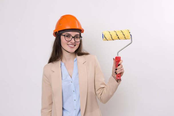 Chica ingeniera en un casco de construcción naranja con herramientas de pintura enlucido en sus manos sobre un fondo blanco. - Foto, Imagen