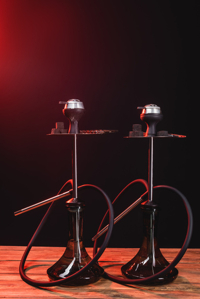 Hookahs on wooden surface on black background with red light - Photo, Image