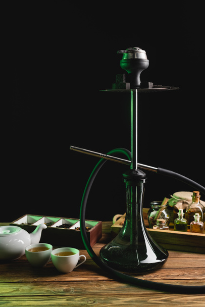 Hookah near tea on wooden table isolated on black  - Foto, afbeelding
