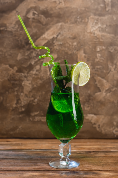 Glass of green cocktail with drinking straw on wooden surface on textured stone background  - Photo, Image