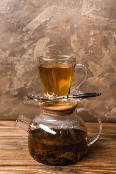 Cup of tea on glass teapot on wooden surface on textured stone background  - Foto, Imagen