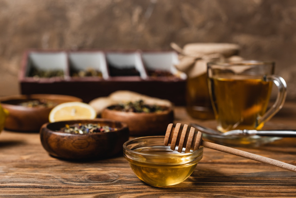 Bowl with honey near blurred tea on wooden surface on brown background  - Foto, Bild