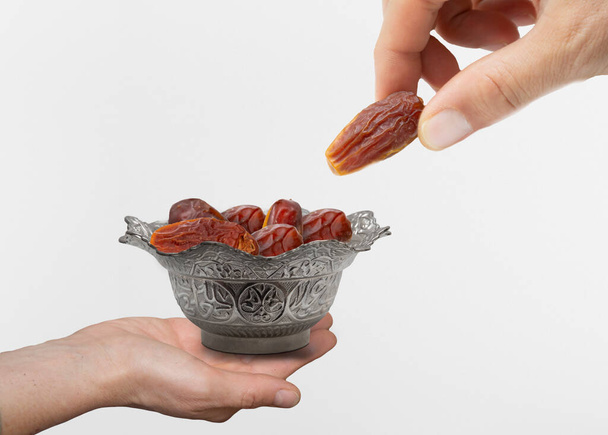hand giving date fruit. Vintage metal bowl full of pitted date fruits on wooden table.  Traditional iftar food. Symbolizing Ramadan. - Photo, Image