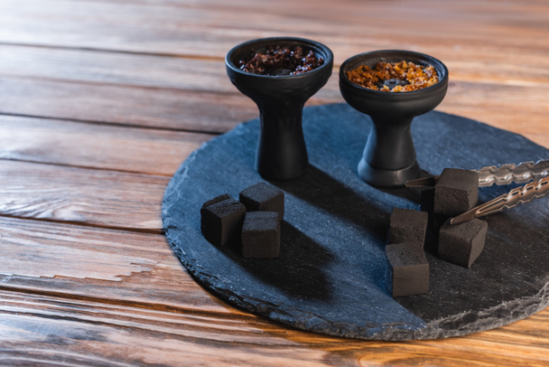 Tweezers near coals and hookah bowls on wooden surface - Fotoğraf, Görsel