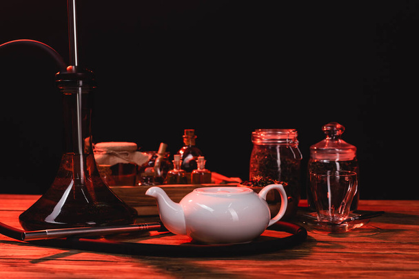 Кальян рядом чайник и банки на деревянной поверхности изолированы на черный  - Фото, изображение