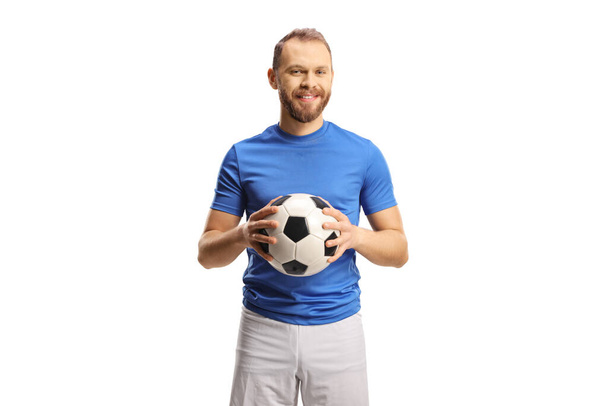 Football player in a blue jersey and white shorts holding a ball and smiling isolated on white background - Foto, Imagem