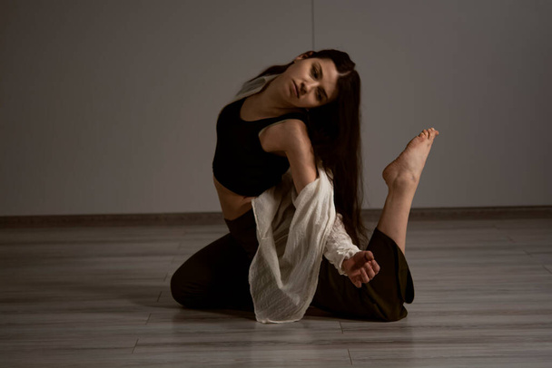 Foto de la joven bailarina rubia en pantalones vaqueros azules rasgados sobre fondo marrón en el estudio - Foto, imagen