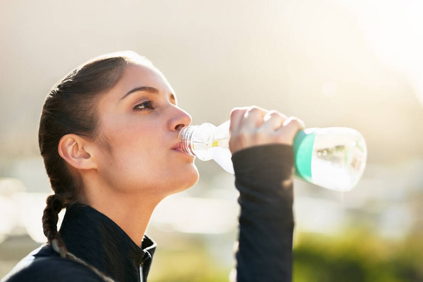 Mantente hidratado. Tiro de una atractiva joven bebiendo agua durante su entrenamiento. - Foto, Imagen