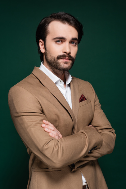 young man with mustache standing with crossed arms on dark green - Fotografie, Obrázek