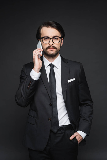スーツ姿のビジネスマンや暗い灰色のスマートフォンで話しているメガネのビジネスマン - 写真・画像