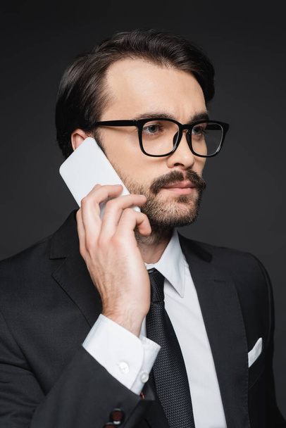 jeune homme d'affaires avec moustache parlant sur smartphone sur gris foncé - Photo, image