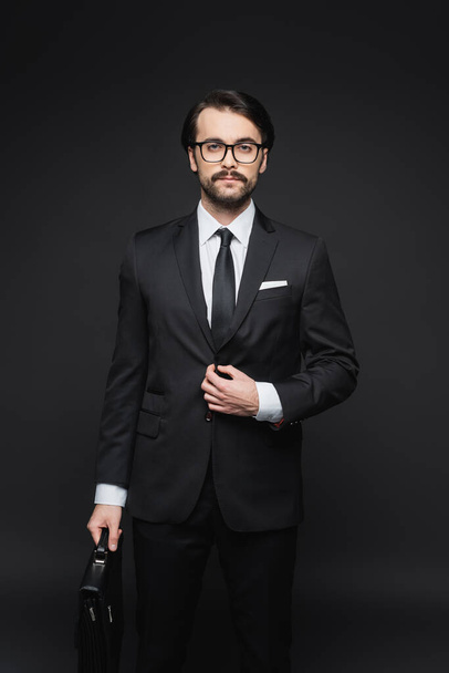 businessman in suit and glasses holding leather briefcase on dark grey - Foto, afbeelding