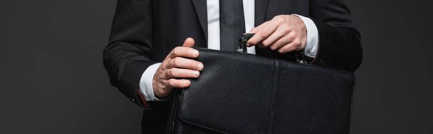 cropped view of businessman in suit holding leather briefcase on dark grey, banner - Foto, afbeelding