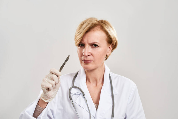 Female plastic surgeon with scalpel look at camera - 写真・画像